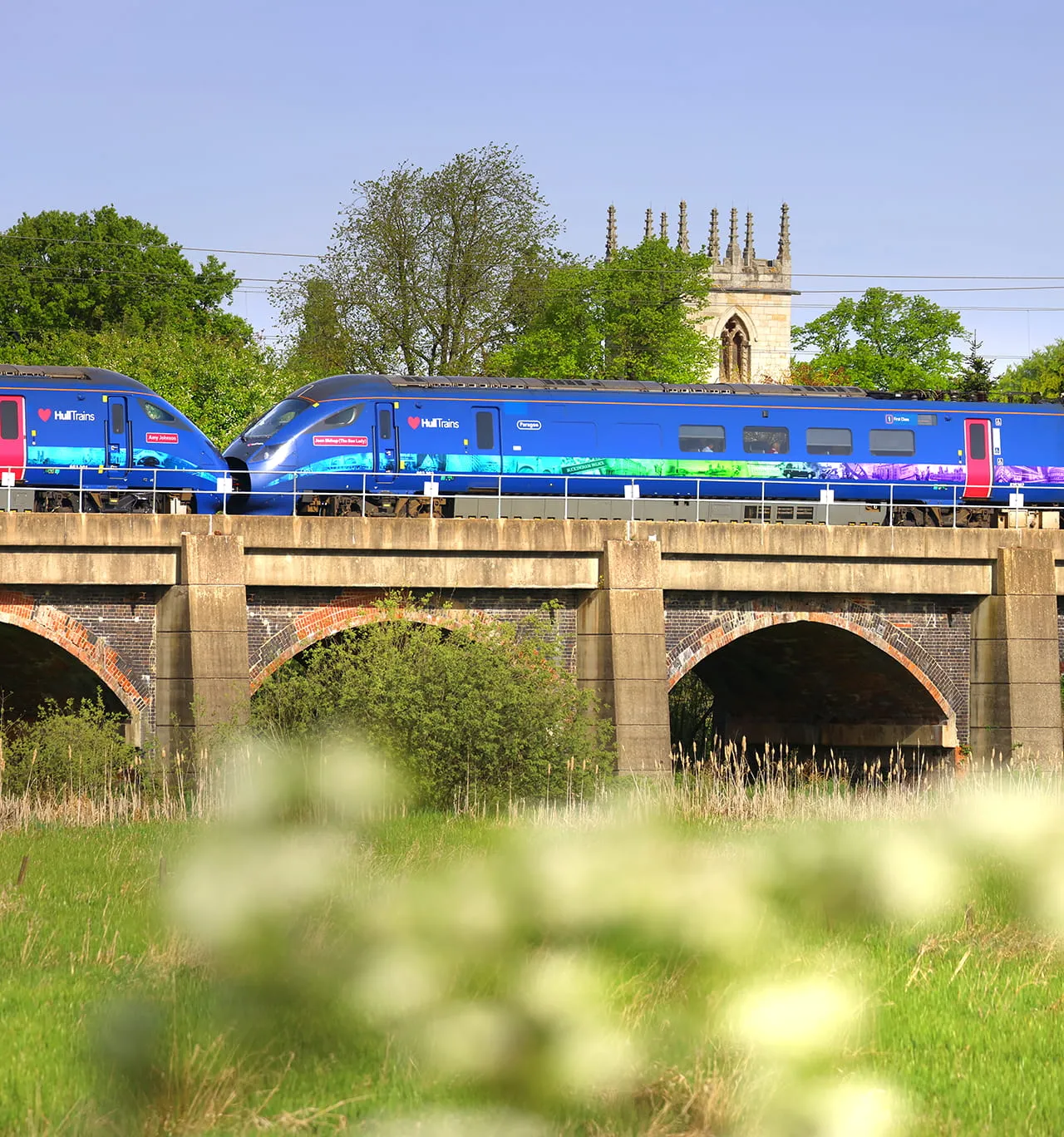 A photo of a train passing over a bridge with a church building in the background